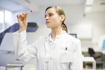 Junge Frau in Laborkittel betrachtet Proberöhrchen