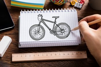 Blick von oben auf eine Hand an einem Notizblock, auf dem ein Fahrrad gezeichnet ist