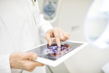 Eine Person hält ein Tablet mit dem Bild eines Gehirnscans.