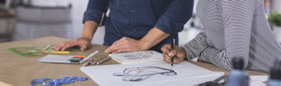 Zwei Produktdesigner arbeiten an einem Designtisch und zeichnen auf einem Block