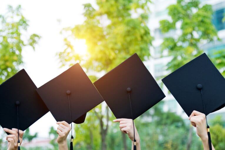 Absolventen halten Doktorhüte hoch