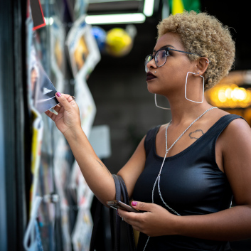 Junge Frau mit Handy checkt Magazine an einem Kiosk