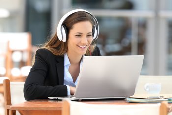 Junge Frau sitzt mit Kopfhörern in Cafe vor Laptop und lächelt