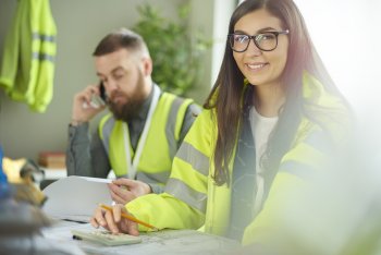 Zwei junge Menschen mit Warnschutzjacken sitzen in einem Büro