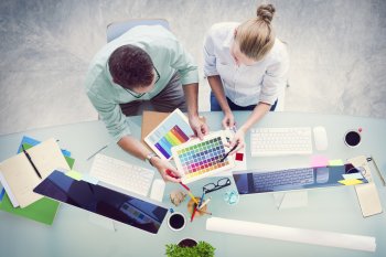 Blick von oben auf zwei Designer, die mit Farbpalette in der Hand am Computer sitzen