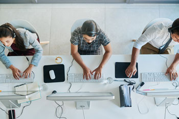 Draufsicht auf drei junge Personen, die an Computern arbeiten.