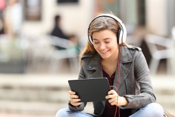 Digitale Medien Studium Medienstudentin sitzt mit Tablet und Kopfhörern draußen und lächelt