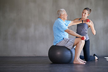 Eine junge Frau führt Übungen mit einem älteren Mann auf einem Gymnastikball durch.
