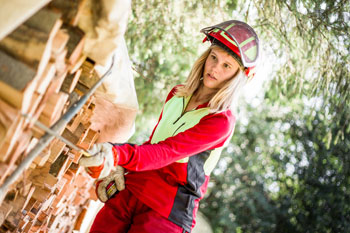 Eine junge Frau in Schutzkleidung betrachtet gestapeltes gefälltes Holz.