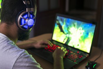 Junger Game Design Student sitzt mit Kopfhörern vor Laptop und spielt