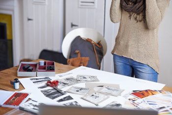 Junge Frau steht vor Tisch, auf dem Bilder und Fotos wild verstreut liegen