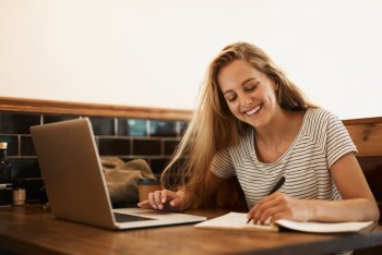 Junge Frau sitzt am Laptop und macht sich Notizen