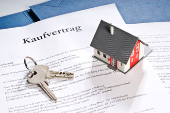 Ein Kaufvertrag mit Hausschlüsseln und einem Miniaturmodell eines Hauses