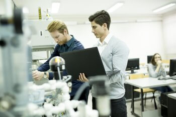 Zwei Ingenieurstudenten stehen mit Laptop an Maschine