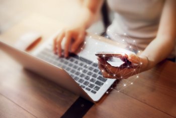 Junger Mann mit Laptop auf dem Schoß und Smartphone in der Hand