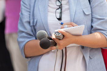 Eine Frau hält zwei Mikrofone und ein Aufnahmegerät und macht sich Notizen.