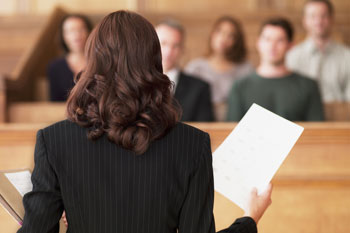 Eine Anwältig spricht mit Papieren in den Händen vor einer Jury.