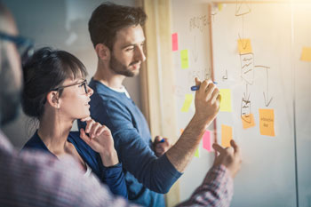 Drei junge Personen diskutieren ein Konzept an einem Whiteboard.