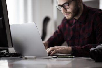 Junger Mann sitzt an Laptop und tippt