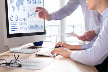 Zwei Personen arbeiten an einem Computer mit Aktienkursen und Diagrammen auf dem Bildschirm.