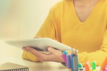 Junge Frau sitzt mit Tablet in der Hand am Tisch