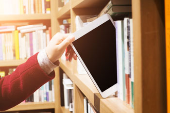 Eine Hand nimmt ein Tablet aus einem Bücherregal.