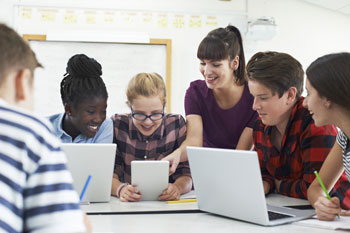 Eine junge Frau hilft Jugendlichen bei der Arbeit mit Notebooks und Tablets.