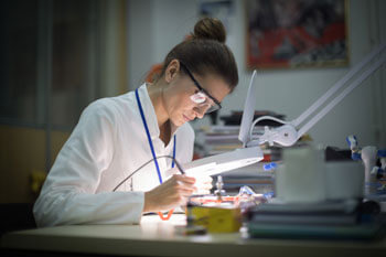 Frau arbeitet an einem elektronischen Gerät unter einem Vergrößerungsglas.