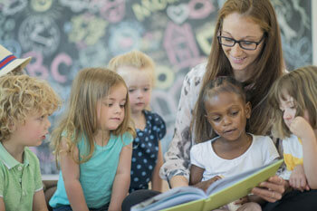 Ein Pädagogin zeigt einer Gruppe von Kindern etwas in einem Buch.