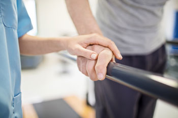 Physiotherapeutin berührt die Hand eines Patienten, der Gehübungen macht.