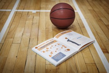 Basketball liegt mit aufgeschlagenem Buch auf Boden der Sporthalle