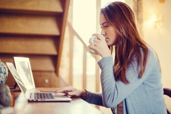 Studentin sitzt mit Kaffeetasse an Laptop