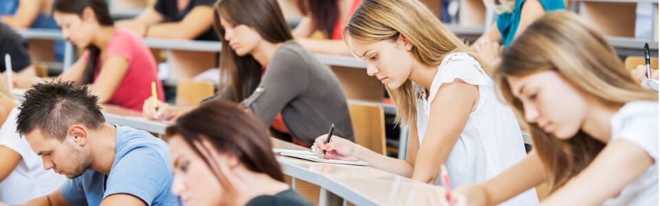 Studierende sitzen im Hörsaal und schreiben Notizen in ihre Hefte