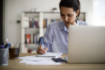 Frau arbeitet am Laptop und macht Notizen